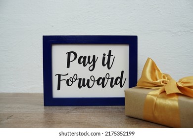 Pay It Forward Text And Gift Box On Wooden Table And White Wall Background