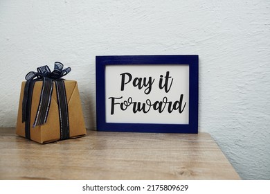 Pay It Forward Text And Gift Box On Wooden Table And White Wall Background