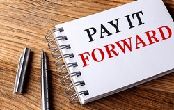 PAY IT FORWARD Text On A Notebook With Pen On Wooden Background