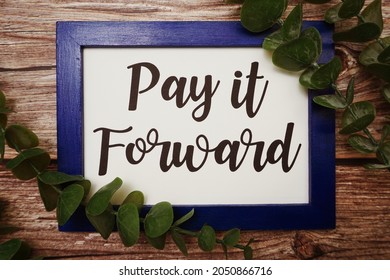 Pay It Forward Written On Blue Frame With Green Leave Flat Lay On Wooden Background