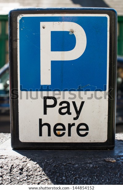 Pay Here signboard on top of an
exterior wall with parked cars visible behind, closeup
view