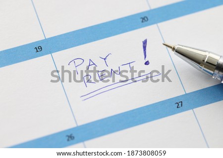 Pay rent is written on sheet of calendar with ballpoint pen closeup. Reminder sticky notes concept