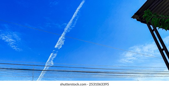 Payakumbuh. September 22th, 2024. A clear blue sky with white contrails intersecting power lines and several power lines stretch diagonally across the sky, creating a grid-like pattern. - Powered by Shutterstock