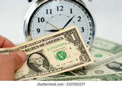 Paying American money banknote currency bills, USA dollars with a blurred alarm clock timer in hours, minutes and seconds scale in the background, paying money for time, time is money concept - Shutterstock ID 2157025277