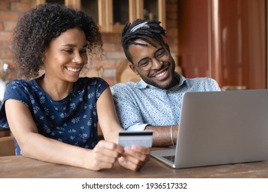 Paying online. Smiling young married couple of afro american ethnicity provide payment via electronic bank app from home office. Happy black spouses buy goods service at web use money on prepaid card