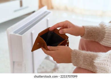 Payment of bills. Cold winter and rising prices for heating, natural gas and electricity. Crisis concept. Female hands hold empty wallet near the radiator - Shutterstock ID 2215707099