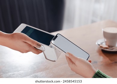 Payment by NFC phone. A woman pays contactlessly using a phone with NFC technology. Wireless money transactions. Card machine in a woman's hand on the background of a cafe - Powered by Shutterstock