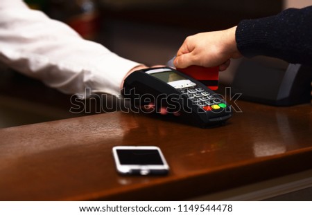 Payment with credit card. Male hand puts bankcard into reader on defocused background. Credit card terminal for cashless payments near mobile phone. Electronic finance and shopping concept.