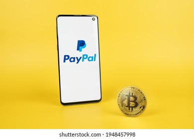 PayPal Logo On Phone Screen With Bitcoin Cryptocurrency Coin On Yellow Background. Checkout With Crypto, Pay Pal New Payment Option Concept. SWANSEA, UK - MARCH 31, 2021