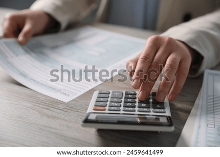 Payroll. Woman using calculator while working with tax return forms at wooden table, selective focus
