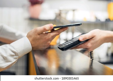 Pays contactless by phone through a terminal in a coffee shop. A young male restaurant employee sells to a customer. Small private business in the city center. - Shutterstock ID 1890301465