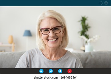 Pc screen view head shot 50s woman wear glasses looking at webcam seated on sofa at home chatting with adult children relatives friends by video conference app. Communication online video call concept