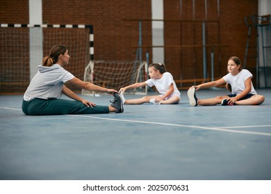 PE Teacher And Her Students Warming Up And Stretching Their Legs On A Class At Elementary School Gym. 