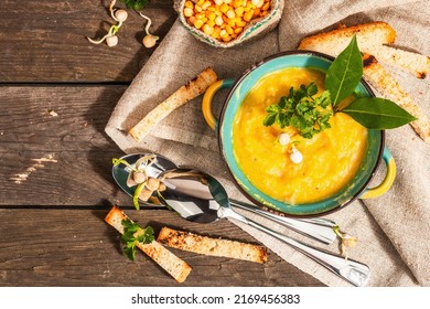 Pea cream soup in a bowl on vintage wooden background. Dry legumes, toast, croutons and greens. Delicious vegan healthy food. A trendy hard light, dark shadow, rustic style, top view