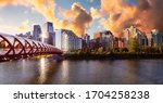 Peace Bridge across Bow River with Modern City Buildings in Background during a vibrant summer sunrise. Cloudy Sky Composite. Taken in Calgary, Alberta, Canada.