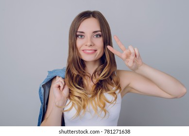 Peace to everybody! Close up portrait of cheerful glad beautiful pretty with curly wavy long perfect hair white t-shirt keeping denim shirt on shoulder demonstrating v-sign isolated on gray background