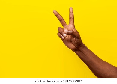 peace gesture on yellow isolated background, african american man's hand shows v-shaped symbol and number two, close-up