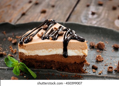 Peace of layered souffle dessert with chocolate sauce on black plate with mint leaves, on blurred wooden table - Shutterstock ID 450399007
