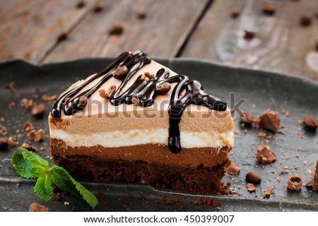 Peace of layered souffle dessert with chocolate sauce on black plate with mint leaves, on blurred wooden table