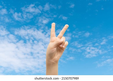 Peace sign gesture made by child on idyllic blue sky background. World peace concept.