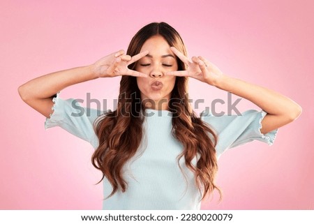 Peace sign, kiss and face of woman in studio for happiness, satisfaction and positive gesture. Silly, goofy and gen z with female isolated on pink background for confidence, pride and emoji symbol