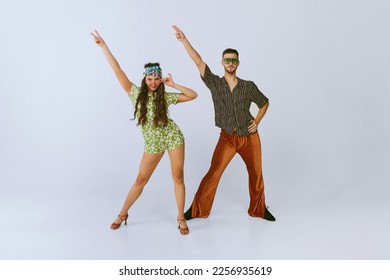 Peace. Stylish young man and woman in fashionable retro outfits dancing disco dance, posing isolated over grey studio background. 70s fashion, hobby, creativity, hippie lifestyle, American culture