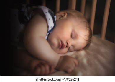 Peaceful Adorable Baby Sleeping On His Bed In A Room At Night. Soft Focus. Sleeping Baby Concept. 1 Year-old Babyboy Sleeps At Home, Dark Background With Light From The Lamp