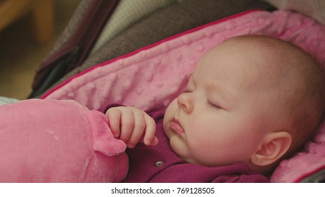 Peaceful Baby Sleeping In A Car Seat On Pink Blanket Holding Hand On A Pink Toy