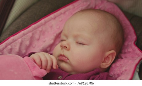 Peaceful Baby Sleeping In A Car Seat On Pink Blanket Holding Hand On A Pink Pig