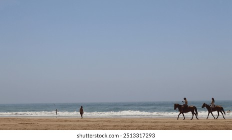 A peaceful beach scene in Agadir, Morocco, with two horseback riders along the shore. Gentle waves and a clear sky complete the serene atmosphere, with distant figures enjoying the water. - Powered by Shutterstock