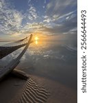 A peaceful beach scene with a hammock gently swaying as the sun sets, casting a warm glow across the water and reflecting in the calm, serene sea.