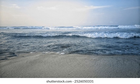 A peaceful beach scene where small waves are gently reaching the shoreline. The sand is light and smooth, with a few patches of moss-covered rocks scattered near the water's edge. - Powered by Shutterstock