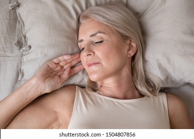 Peaceful Beautiful Mature Woman Sleeping In Bed In The Morning Close Up, Relaxed Older Female With Closed Eyes Lying On Soft Pillow Top View, Resting In Bedroom, Enjoying Fresh Bedclothes