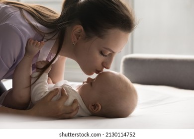 Peaceful Beautiful Young Mom Calming, Comforting Baby Resting On Back On Bed, Kissing Kids Forehead, Head With Love, Tenderness, Care, Caressing Sleepy Child. Motherhood, Parenting Concept