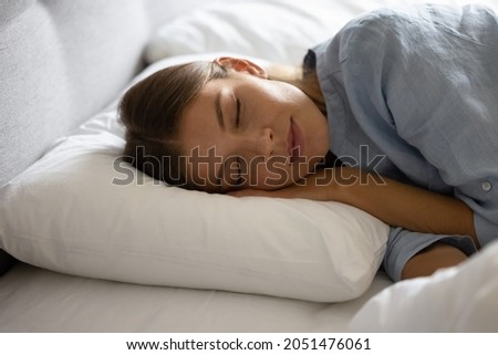 Peaceful calm girl sleeping in soft linen comfortable beddings, lying on orthopedic mattress with head resting on pillow, smiling with closed eyes. Young woman enjoying bedtime recreation, relaxation
