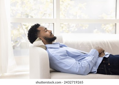 Peaceful calm young African American man lying on white couch, relaxing with closed eyes, sleeping at daytime, breathing fresh air, enjoying leisure, silence, calmness, work break - Powered by Shutterstock