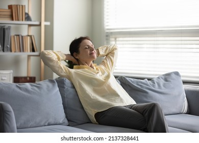 Peaceful Cheerful Lady Enjoying Leisure Time, Emotional Harmony At Home, Breathing Fresh Cool Purified Air, Resting On Couch With Closed Eyes. Senior Homeowner Woman Relaxing In Living Room