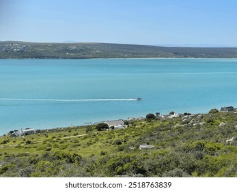 A peaceful coastal landscape featuring a turquoise bay, a motorboat cruising across calm waters, and scattered homes on green hills. Ideal for travel, nature, or ocean scenery projects with a serene v - Powered by Shutterstock