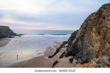 A peaceful coastal scene at sunset with a solitary figure walking on the sandy beach. The waves gently lap the shore, and towering cliffs frame the coast of Portugal. - Powered by Shutterstock - Get 15% off with code: PIKWIZARD15