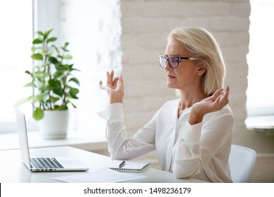 Peaceful Concentrated Senior Businesswoman Sit At Office Desk Meditating At Workplace, Calm Focused Aged Woman Worker With Mudra Hands Practice Yoga Manage Emotions. Stress Free Concept