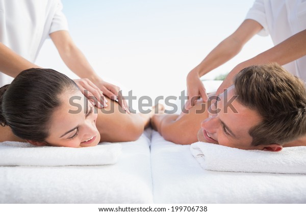 Peaceful couple enjoying couples massage poolside\
outside at the spa