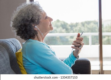 Peaceful Elderly Woman Wearing Earphones Enjoying Music. Side View Of Senior Grey Haired Lady Using Smartphone For Songs Listening. Music Therapy Concept
