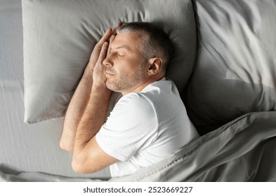 Peaceful European middle aged man sleeping on side in bed at home, enjoying his comfortable pillow and mattress, top above view. Healthy, good sleeping - Powered by Shutterstock