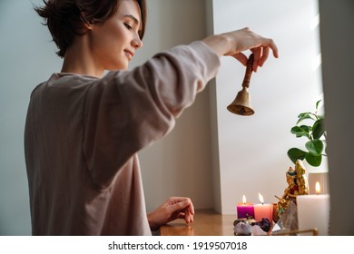 Peaceful Girl Ringing Bell While Praying At Home Shrine Indoors