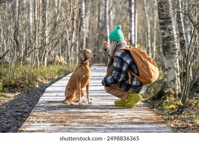 Peaceful girl traveler holding treat reward in hand, training dog giving commands waiting for execution. Pet obediently fulfills requirements, looking lovingly at owner. Woman, puppy in autumn woods. - Powered by Shutterstock