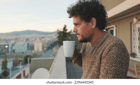 Peaceful guy looks at the city from the balcony and drinks coffee, enjoys the beautiful view - Powered by Shutterstock