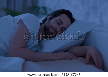 Peaceful handsome bearded young man sleeping in comfortable bed alone at home, enjoying his orthopedic mattress and pillow, side view, copy space. Good sleep concept