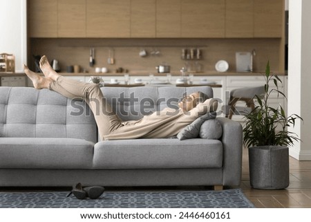 Peaceful happy mature woman lying on sofa relax in living room, enjoy lazy weekend at home, dreaming, smile, breathing fresh air, feel carefree, resting after working day on comfortable couch. Pastime
