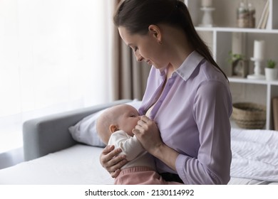 Peaceful Happy Mom Breastfeeding Baby At Home. Young New Mother Holding And Feeding Newborn Child Milk From Breast, Caring Of Infant Healthy Nutrition, Looking At Son, Daughter, Smiling