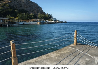 A peaceful harbor reveals its beauty at dawn, with soft waves gently lapping against the stone pier, surrounded by lush greenery and clear blue waters. - Powered by Shutterstock